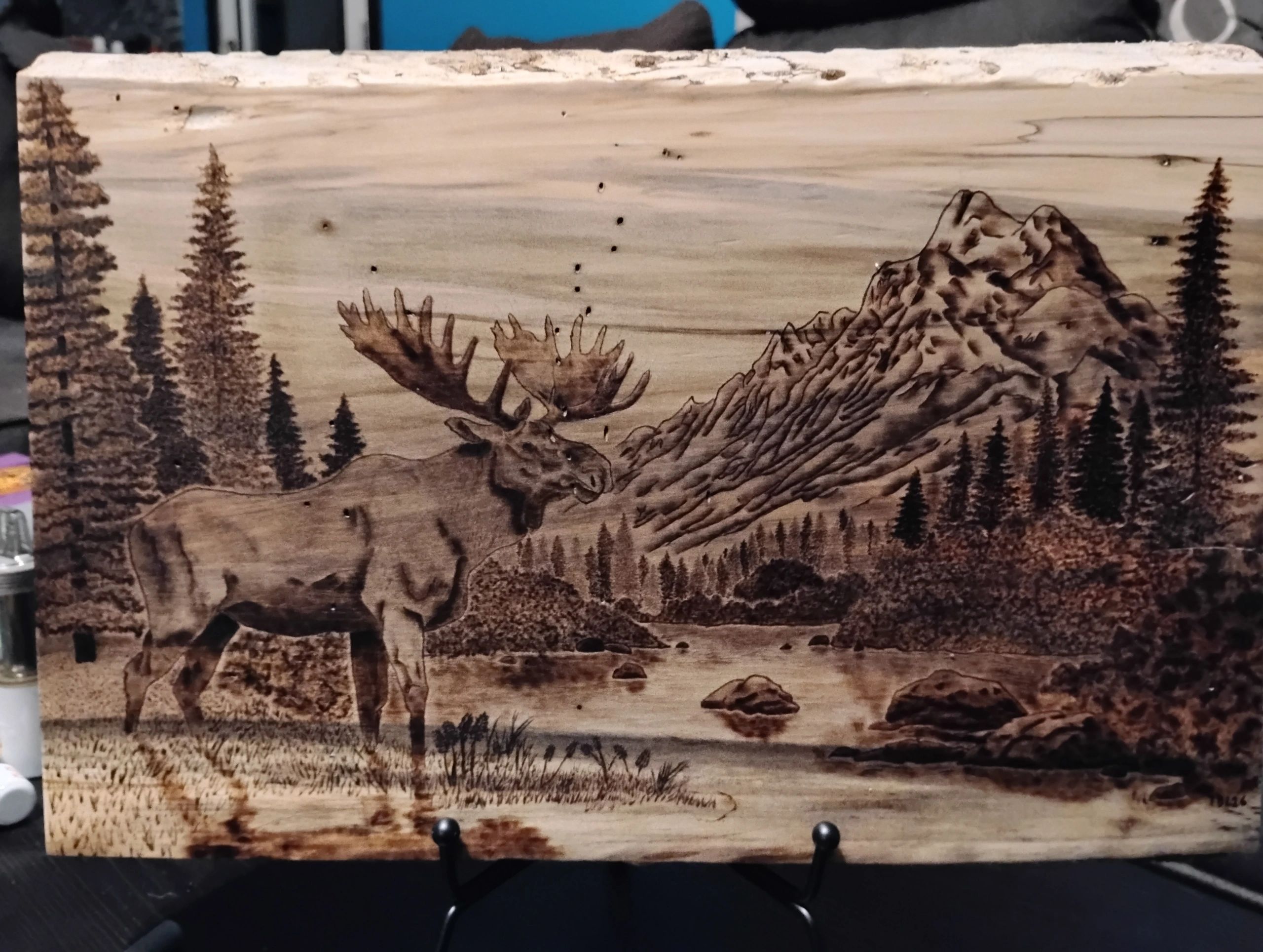 Elk beside a mountain lake and pine forest, burned into a wood slab